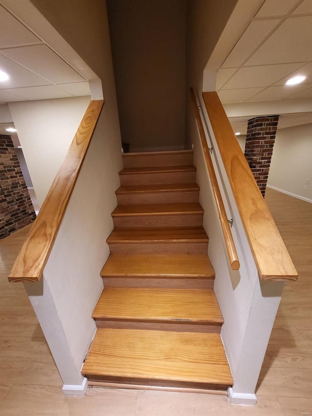 stairway featuring hardwood / wood-style flooring, brick wall, and a paneled ceiling