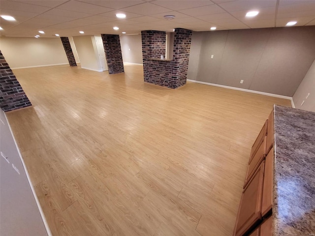 basement with brick wall, light hardwood / wood-style floors, and a drop ceiling