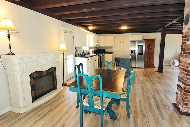 dining space featuring brick wall, a fireplace, light wood-type flooring, beamed ceiling, and sink