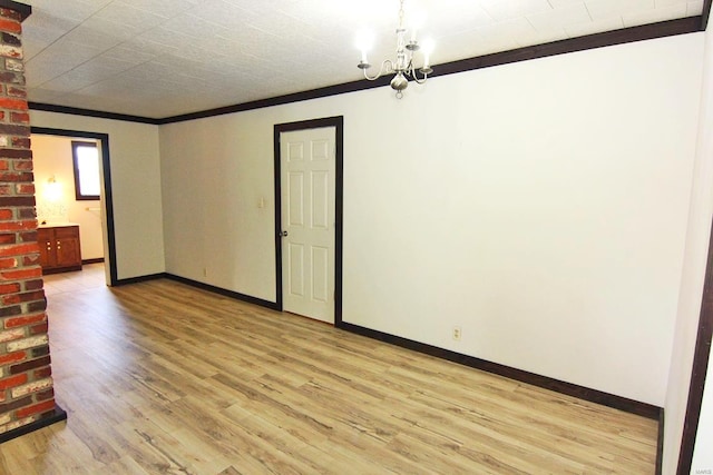 spare room with brick wall, light wood-type flooring, and an inviting chandelier