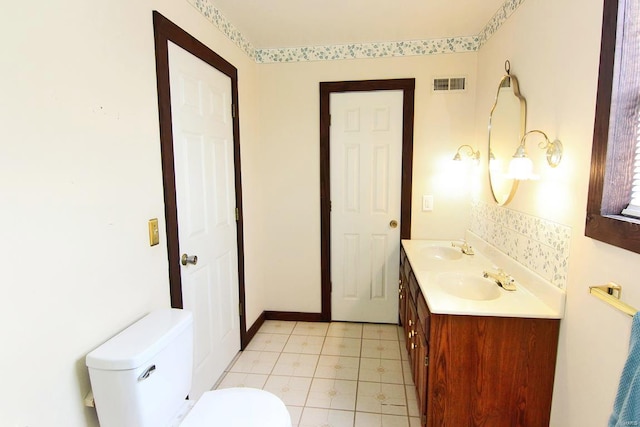 bathroom with double vanity, visible vents, toilet, and a sink