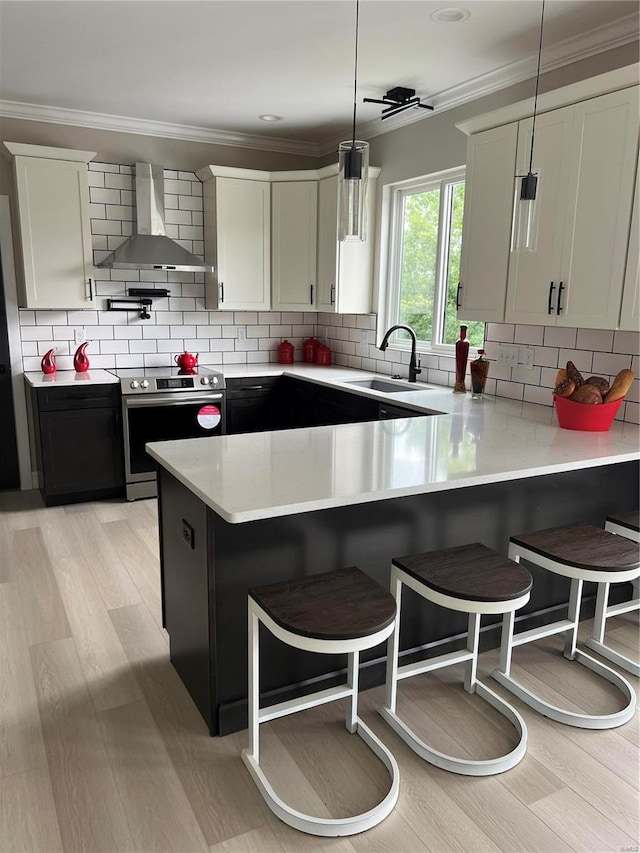 kitchen featuring electric stove, white cabinetry, pendant lighting, and wall chimney range hood