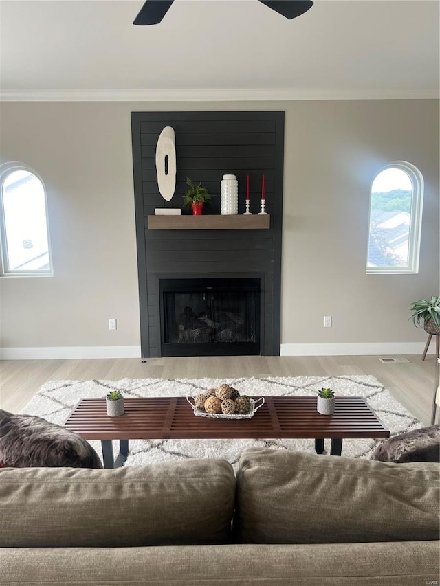 living room with a large fireplace, crown molding, plenty of natural light, and hardwood / wood-style flooring