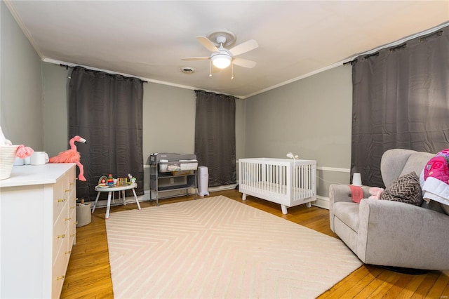 bedroom featuring ceiling fan, a nursery area, ornamental molding, and light hardwood / wood-style flooring