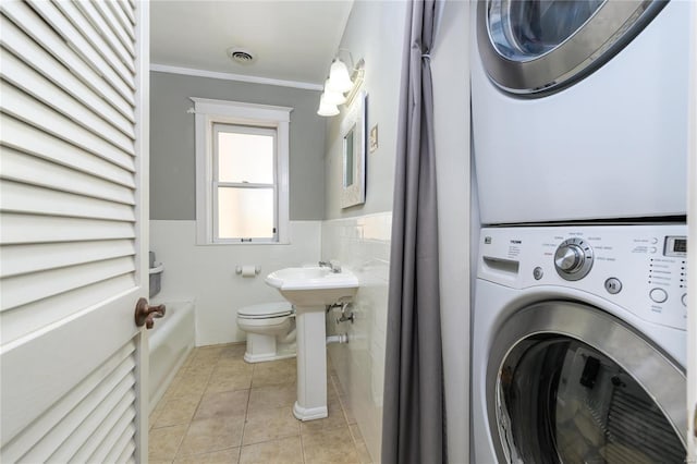 clothes washing area with stacked washing maching and dryer, light tile patterned floors, and ornamental molding