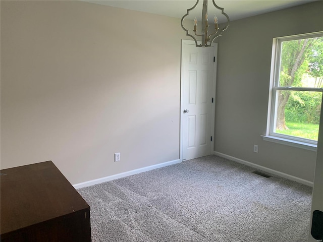 spare room featuring carpet and an inviting chandelier