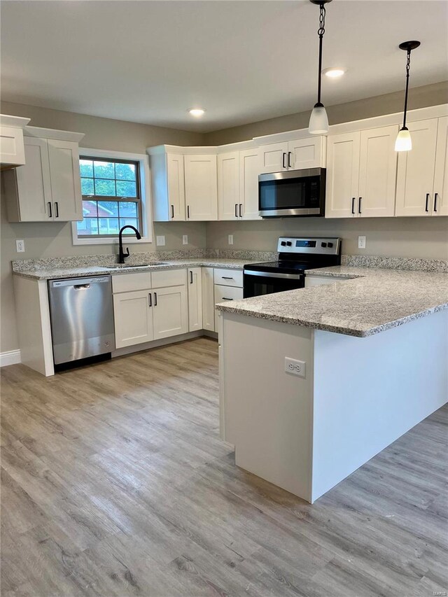 kitchen with light wood-type flooring, appliances with stainless steel finishes, decorative light fixtures, and white cabinetry