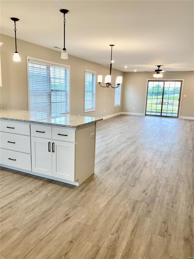 kitchen with white cabinetry, light stone countertops, pendant lighting, and light wood-type flooring