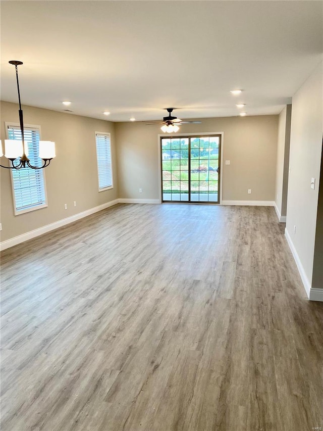 unfurnished living room with wood-type flooring and ceiling fan with notable chandelier