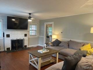 living room with a brick fireplace, ceiling fan, and dark wood-type flooring