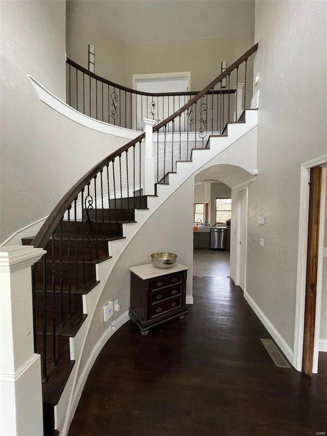 stairs with dark wood-type flooring and a towering ceiling