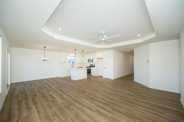 unfurnished living room featuring ceiling fan with notable chandelier, light hardwood / wood-style floors, and a tray ceiling