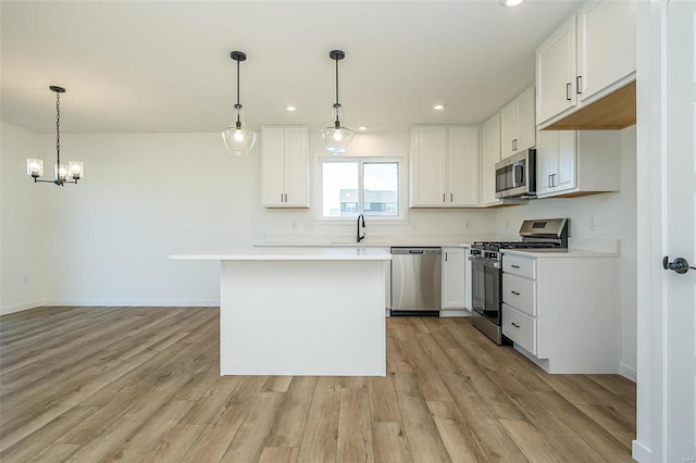 kitchen with decorative light fixtures, light wood-type flooring, white cabinetry, and appliances with stainless steel finishes