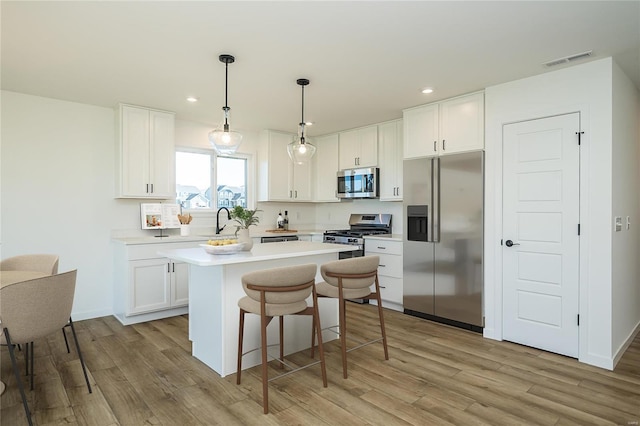 kitchen with white cabinetry, hanging light fixtures, appliances with stainless steel finishes, and light hardwood / wood-style flooring