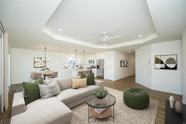 living room with ceiling fan with notable chandelier, a tray ceiling, and light hardwood / wood-style floors