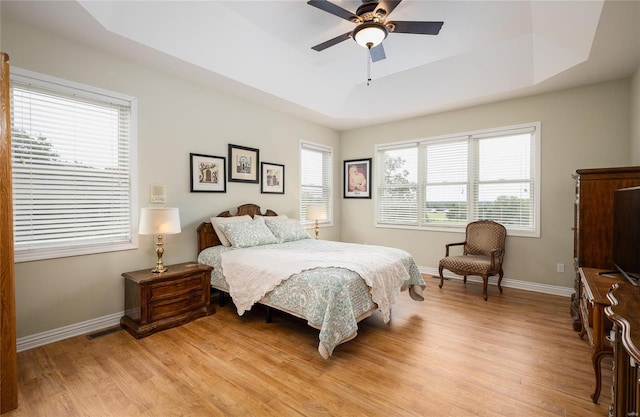 bedroom featuring ceiling fan, a raised ceiling, and light wood-type flooring