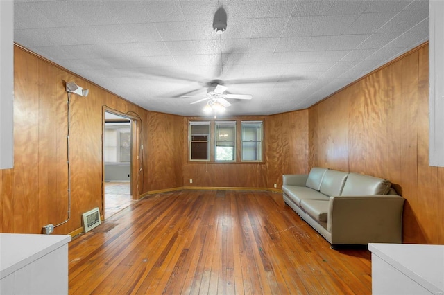 sitting room with ceiling fan, wood walls, and hardwood / wood-style flooring