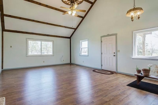 unfurnished living room featuring a towering ceiling, hardwood / wood-style floors, and ceiling fan with notable chandelier