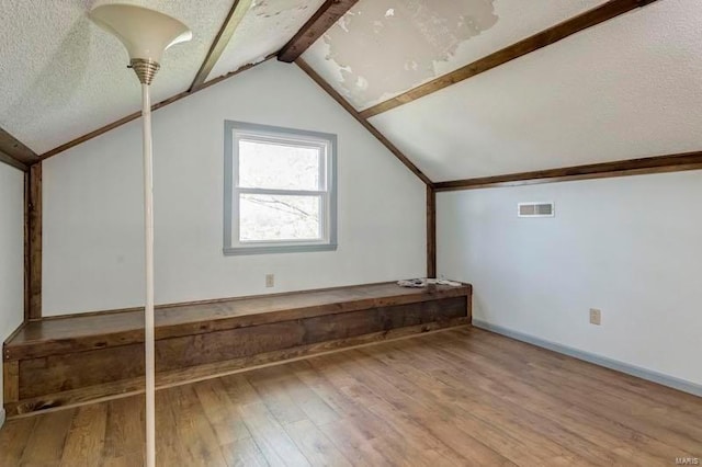 additional living space featuring vaulted ceiling, hardwood / wood-style floors, and a textured ceiling