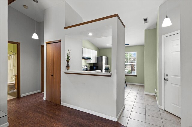 kitchen with kitchen peninsula, light wood-type flooring, decorative light fixtures, black range, and white cabinetry