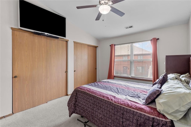bedroom featuring two closets, ceiling fan, light colored carpet, and vaulted ceiling