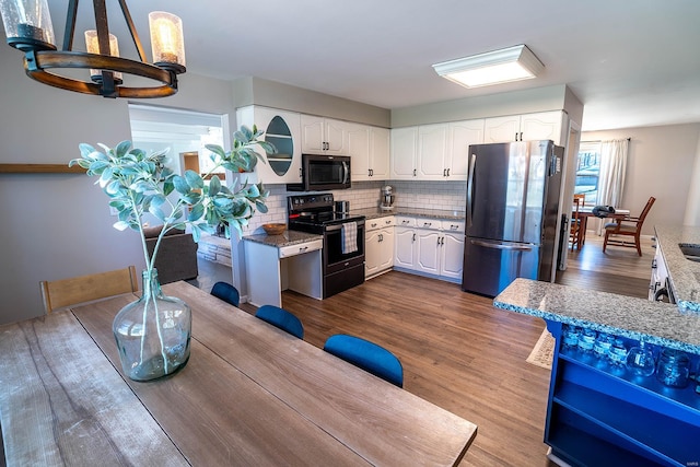 kitchen with black appliances, dark hardwood / wood-style floors, light stone countertops, and white cabinetry