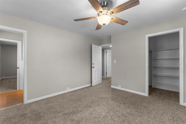 unfurnished bedroom with a walk in closet, a closet, ceiling fan, and carpet flooring