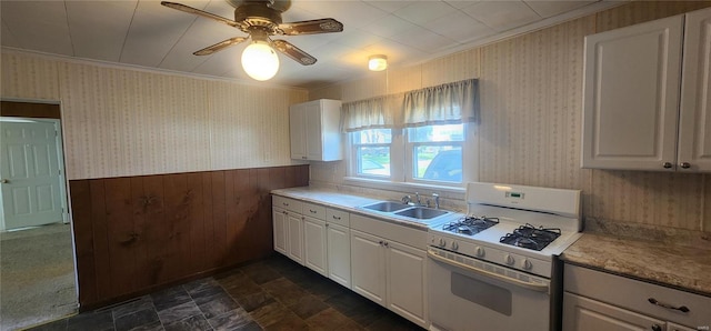 kitchen with white gas stove, ceiling fan, dark tile flooring, white cabinets, and sink