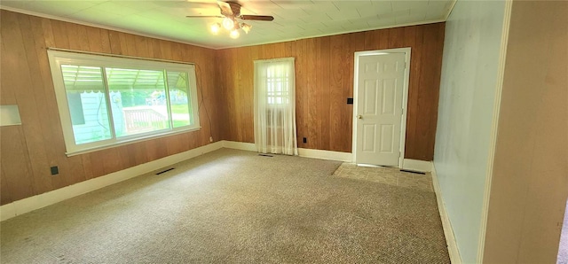 carpeted spare room featuring wooden walls and ceiling fan