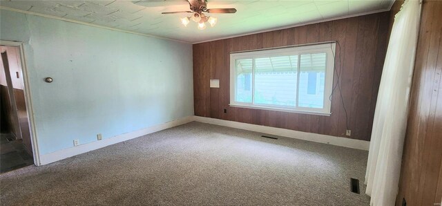 empty room featuring carpet flooring, wood walls, ornamental molding, and ceiling fan