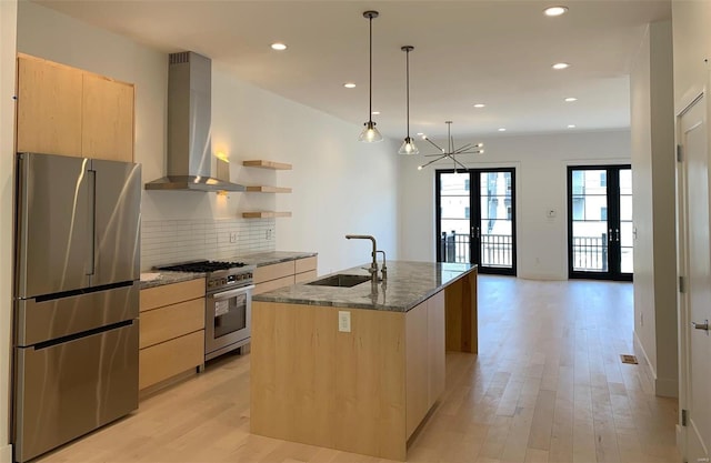 kitchen with sink, wall chimney exhaust hood, stainless steel appliances, french doors, and a center island with sink