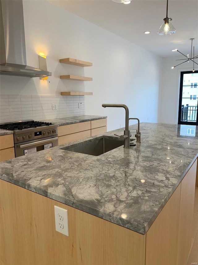 kitchen featuring high end stainless steel range oven, sink, wall chimney range hood, light brown cabinets, and dark stone countertops