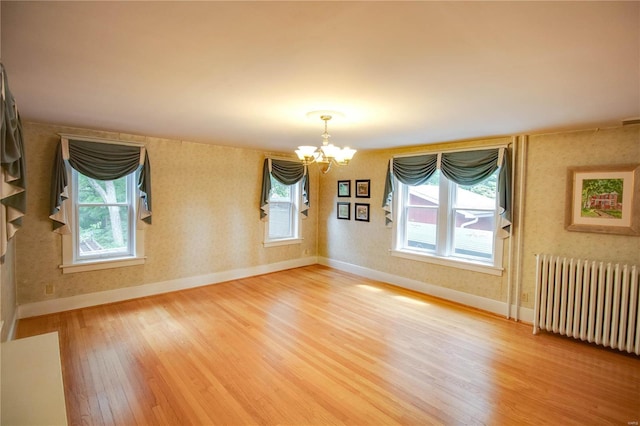 unfurnished room with an inviting chandelier, plenty of natural light, radiator, and hardwood / wood-style floors