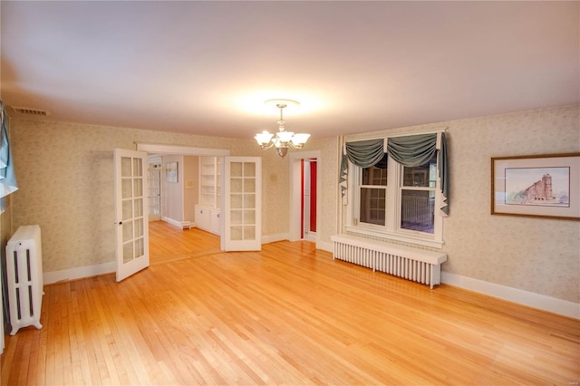 empty room featuring radiator, hardwood / wood-style flooring, a notable chandelier, and french doors