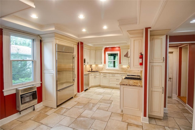 kitchen featuring stainless steel appliances, a tray ceiling, light stone countertops, and heating unit