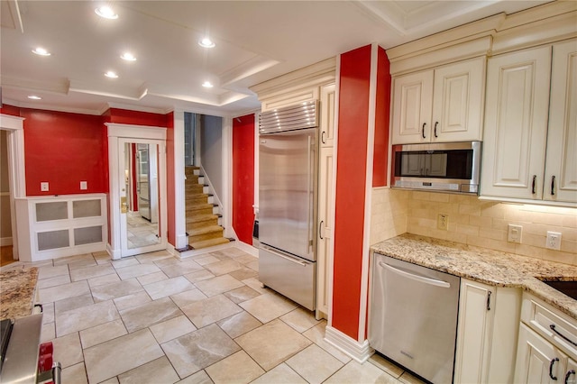 kitchen featuring appliances with stainless steel finishes, a tray ceiling, decorative backsplash, and cream cabinetry