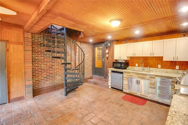 kitchen with sink, light stone counters, stainless steel dishwasher, wooden walls, and brick wall