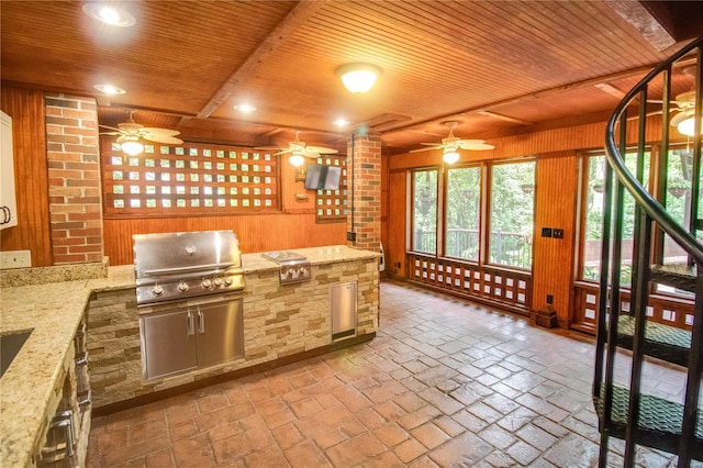 kitchen featuring wood ceiling, ceiling fan, light stone counters, and wood walls