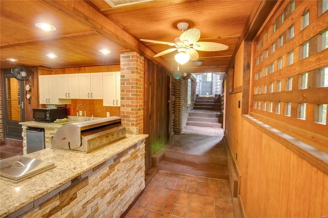 kitchen featuring wood ceiling, white cabinetry, stainless steel dishwasher, wooden walls, and light stone countertops