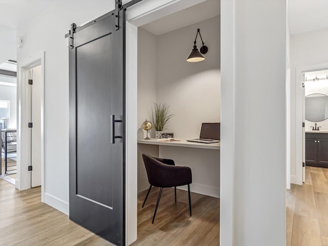 office area with a barn door, sink, and light hardwood / wood-style flooring