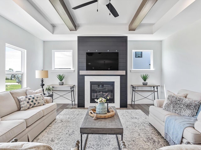 living room with hardwood / wood-style floors, beam ceiling, a wealth of natural light, and a large fireplace