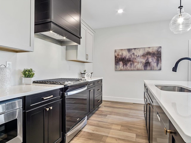 kitchen with stainless steel range with gas cooktop, pendant lighting, white cabinetry, wall chimney range hood, and light wood-type flooring