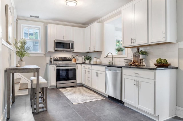 kitchen with dark tile patterned floors, white cabinets, stainless steel appliances, sink, and ornamental molding