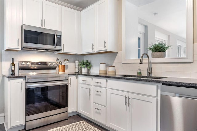 kitchen featuring sink, dark stone counters, stainless steel appliances, and white cabinetry