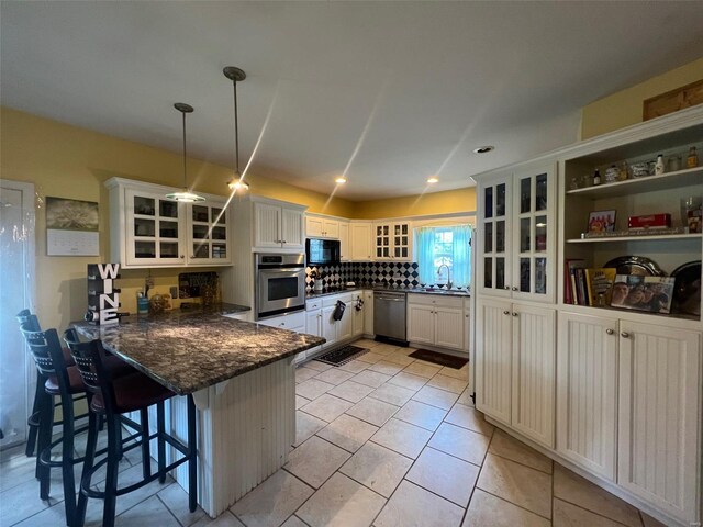 kitchen featuring hanging light fixtures, appliances with stainless steel finishes, backsplash, a breakfast bar, and light tile floors