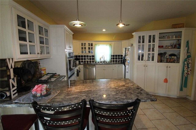 kitchen featuring stainless steel appliances, kitchen peninsula, backsplash, a kitchen bar, and light tile floors