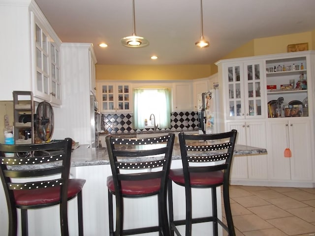 kitchen with white refrigerator, white cabinets, backsplash, a breakfast bar, and light tile floors