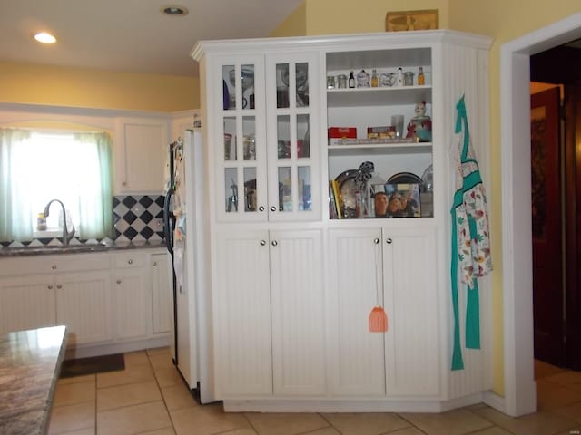 kitchen featuring white refrigerator, tasteful backsplash, dark stone countertops, sink, and light tile floors