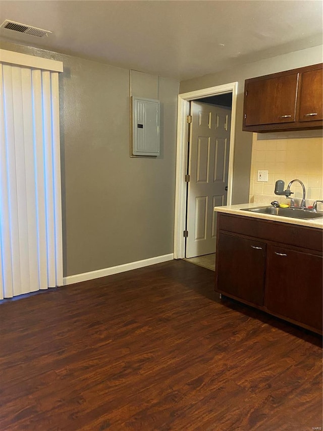 kitchen with dark brown cabinetry, dark hardwood / wood-style flooring, electric panel, and sink