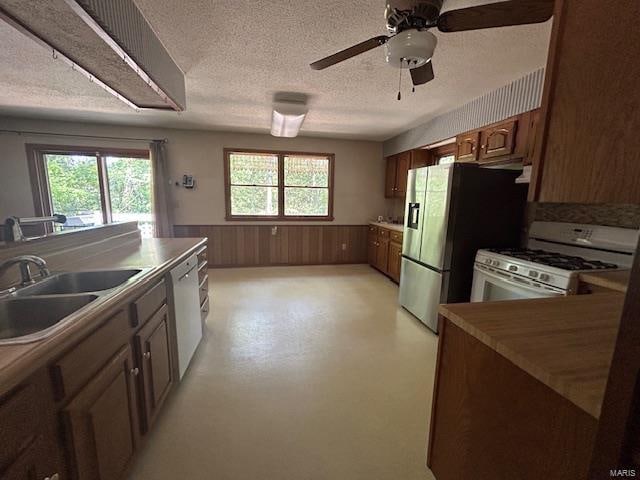 kitchen featuring a textured ceiling, white appliances, ceiling fan, sink, and wood walls